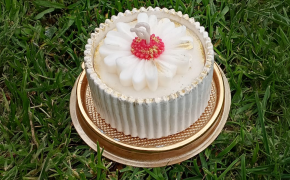 Vela cilíndrica blanca con base dorada y decoración floral en la parte superior