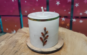 Vela cilíndrica blanca con borde verde y diseño de hojas secas