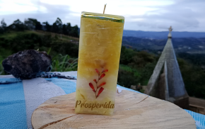 Vela cuadrada amarilla con grabado “Prosperidad” y flores secas