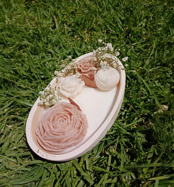Vela decorativa con forma de flor rosada y blanca sobre pasto